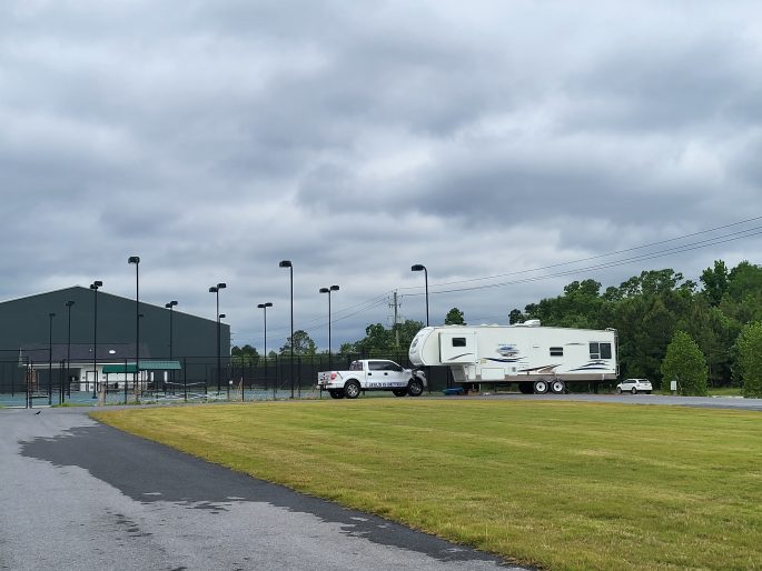 RV and truck on a campground in front of a tennis court 