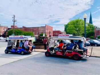 People enjoy a guided golf cart tour through a tree-lined street in the downtown district.