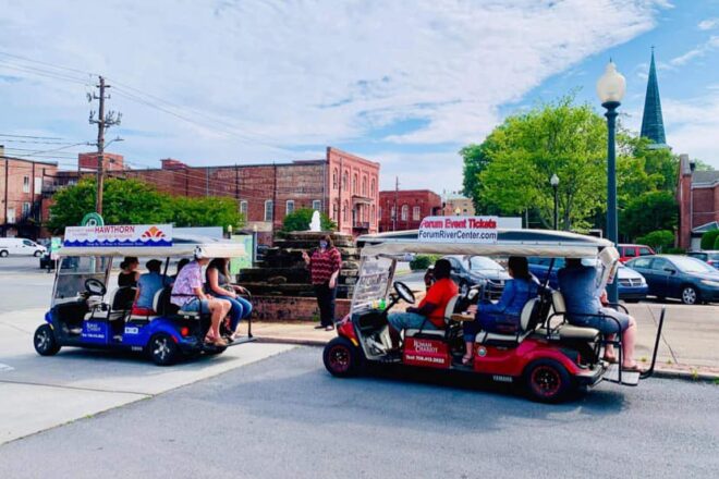 People enjoy a guided golf cart tour through a tree-lined street in the downtown district.