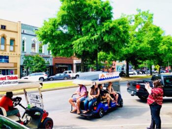 People enjoy a guided golf cart tour through a tree-lined street in the downtown district.