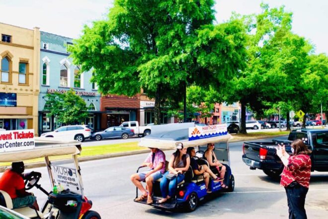 People enjoy a guided golf cart tour through a tree-lined street in the downtown district.
